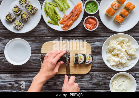 Vista in pianta parziale di persona il taglio di delizioso sushi roll con coltello Foto Stock