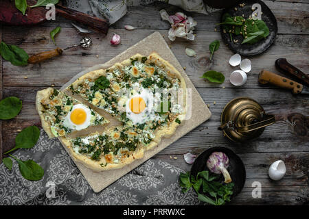 Vista superiore della pizza fatta in casa con le uova e le erbe sul pannello di legno Foto Stock