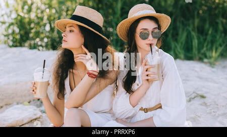 Bellissima femmina amici in cappelli di paglia di bere caffè latte e sedersi sul terreno Foto Stock