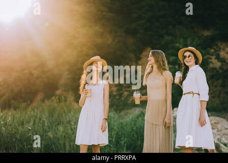 Bellissima femmina amici in cappelli di paglia a piedi nella natura con i bicchieri di plastica di caffè latte Foto Stock