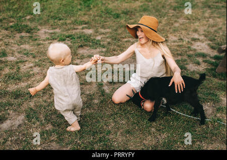 Allegro madre, piccolo figlio e capra domestica su erba verde in campagna Foto Stock