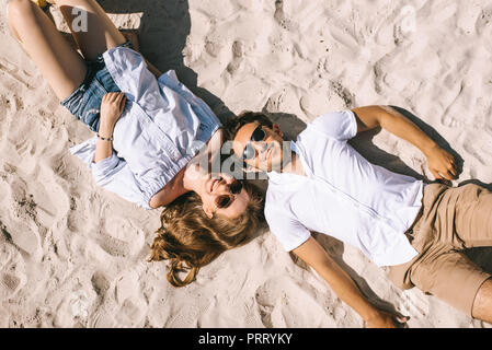 Vista in elevazione della coppia sorridente che giace sulla spiaggia di sabbia della città Foto Stock