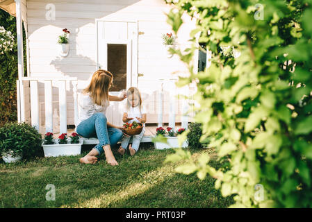 Madre e adorabile ragazzino con coppa di fragole in appoggio sul portico del piccolo paese casa insieme Foto Stock