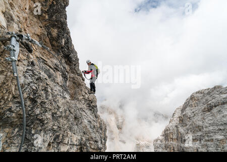 Giovane femmina attraente studentessa universitaria su un piano verticale ed esposta di roccia si arrampica su una via ferrata in Alta Badia in Alto Adige Foto Stock