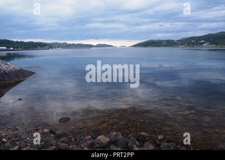 La vista di Lochinver, Scozia oltre al porto e al mare aperto con alghe marine coperta immersa pietre in primo piano Foto Stock