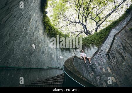 Lonely Man seduto sulla scalinata a spirale dal passaggio pedonale sotterraneo in Singapore. Foto Stock