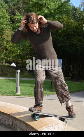 Giovane maschio caucasico lo skateboard in un parco, concentrandosi sul bilanciamento del blu su ruote di skateboard. Foto Stock