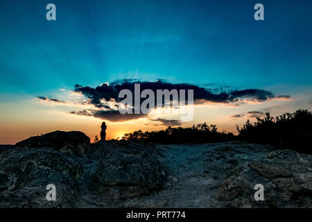 Irriconoscibile silhouette femminile al tramonto colorato con raggi solari contro il sole vicino la pietra di funghi fenomeno naturale nel sud della Bulgaria, vicino alla città di Kardzhali Foto Stock