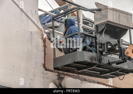 Saldatrice a lavorare su una nave seduto in una gabbia di una gru la saldatura di una piastra in acciaio Foto Stock