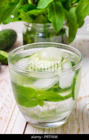 Acqua fresca con il cetriolo, la menta e il ghiaccio in vetreria a vassoio in legno, primo piano. Foto Stock