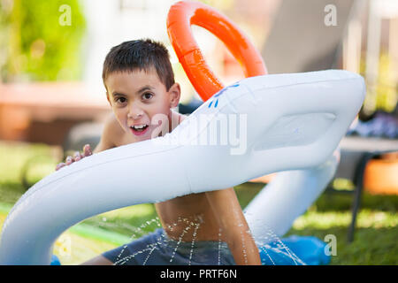 Ragazzo spruzzi in una diapositiva di acqua avendo divertimento durante l'estate in un cortile Foto Stock