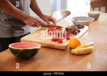 Giovane uomo per affettare frutta fresca al tavolo da cucina, metà sezione Foto Stock