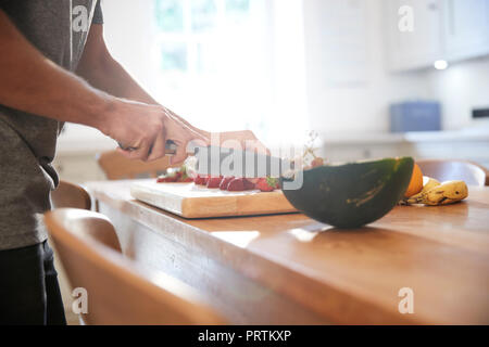 Giovane uomo per affettare frutta fresca al tavolo da cucina, metà sezione Foto Stock