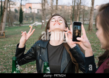 Donna prendendo fotografia di amico equilibratura di tappi di bottiglia su guance Foto Stock