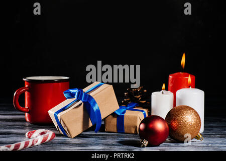 Vista ravvicinata di candele accese, Pigna, palle di Natale e regali sul tavolo di legno su nero Foto Stock