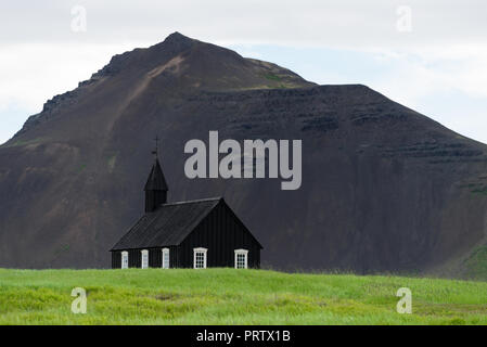 Budakirkja - chiesa nera in Budir village. I religiosi e le attrazioni turistiche dell'Islanda. Cappella sullo sfondo della montagna Foto Stock