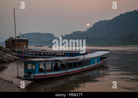 Vista di alcuni tour ormeggiate barche sul fiume Mekong e Chomphet District attraverso il fiume a Luang Prabang, Laos, al tramonto. Foto Stock