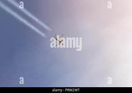 Aereo passeggeri battenti alto nel cielo chiaro lasciando sentieri bianco. Grande aereo durante il tramonto con cielo drammatico sullo sfondo. Viaggi e avia Foto Stock