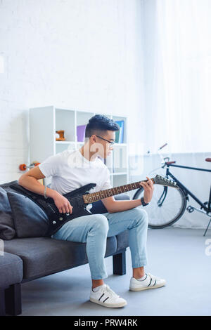 Bel uomo asiatico giocando F principali corda su unplugged chitarra elettrica a casa Foto Stock