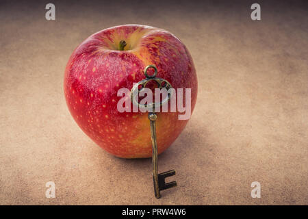 Mano che tiene una chiave accanto a una mela rossa Foto Stock