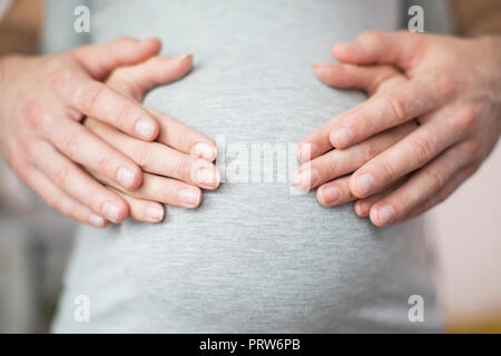 Close Up di maschio e femmina mani appoggiate sulla gravidanza Womans Stomaco Foto Stock