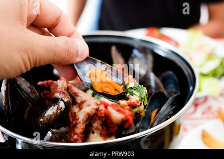 Primo piano di un uomo mangiare alcuni moules a la bonifacienne, una ricetta di cozze tipica di Bonifacio in Corsica, Francia Foto Stock