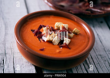 Primo piano di un vaso di terracotta con lo spagnolo salmorejo cordobes o porra antequerana, un freddo minestra di pomodoro, guarnita con prosciutto Serrano e crostini, su un wh Foto Stock