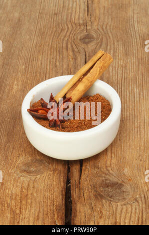 Il cinese cinque spezie in un ramekin con anice stellato e cannella sul vecchio legno stagionato Foto Stock