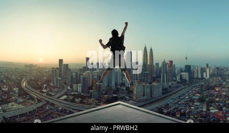 Giovane uomo di saltare sul tetto con grande paesaggio urbano in vista di sunrise. Foto Stock