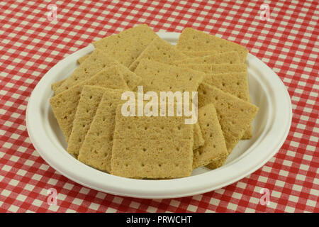 Graham cracker piazze snack su bianco eco-friendly piastra monouso in rosso tovaglia a scacchi Foto Stock