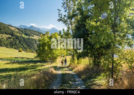 2 persona a piedi verso il basso di una corsia di marcia nei pressi di un vegetale plot (sinistra) di Lignan, Valle d'Aosta, NW Italia Foto Stock