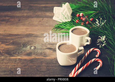 Cioccolata calda in due tazze con connettori lollipop, abete e toy house su sfondo di legno, tonica foto Foto Stock