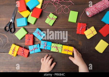 Regalo Pacchetto colorato elaborazione di decorazione con due bambini le mani sul tavolo di legno; laici piana; vista aerea Foto Stock