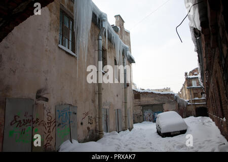 San Pietroburgo, Russia; - Gennaio 5, 2011: enormi ghiaccioli appesi da un tetto di un vecchio edificio; abbandonato auto coperto di neve Foto Stock