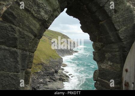 Giugno 2015 - Vista del drammatico Cornovaglia lungo la costa attraverso una pietra infisso di Tintagel Castle rovine, un mitico luogo di nascita del leggendario Re Artù Foto Stock