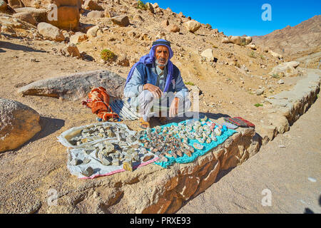 Santa Caterina, Egitto - 25 dicembre 2017: Il senior vendor beduino siede alla strada di montagna e vende souvenir locali - il quarzo geodes e Mou Foto Stock