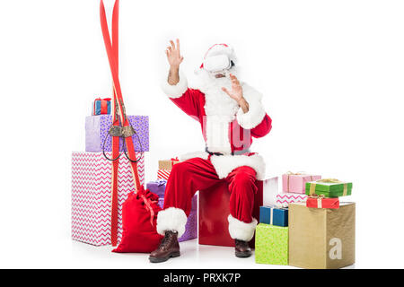 Babbo Natale che indossa la realtà virtuale auricolare e seduta sulla pila di confezioni regalo isolato su sfondo bianco Foto Stock