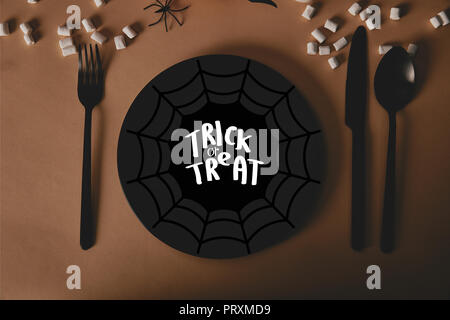 Vista superiore della piastra nera con spider web e "dolcetto o scherzetto" scritte, forchetta e coltello con marshmallows sul tavolo, concetto di halloween Foto Stock