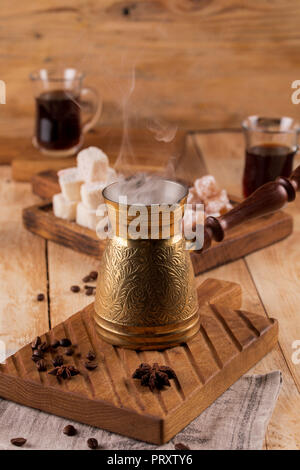 Hot cereali, caffè nero in Turku, con vapore su un sfondo di legno. caffè turco nel tradizionale goffrato metallo turk. Foto Stock