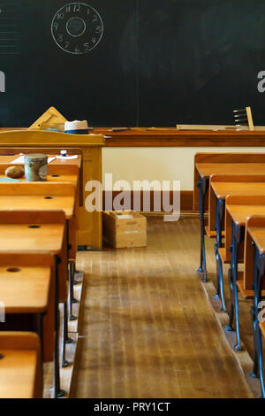 Banchi vuoti in aula scolastica con lavagna in background. Foto Stock