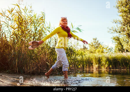 Di mezza età nudi donna camminando sulla riva del fiume sulla giornata d'autunno. Senior lady divertirsi nella foresta e godere la natura Foto Stock