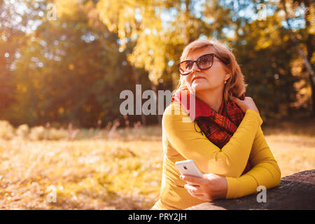 Donna di mezza età tenendo selfie sul telefono passeggiate nel parco. Senior lady gode di natura nella foresta di autunno Foto Stock