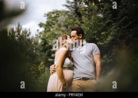 Donna incinta bacia il partner mentre passeggiate nella natura Foto Stock