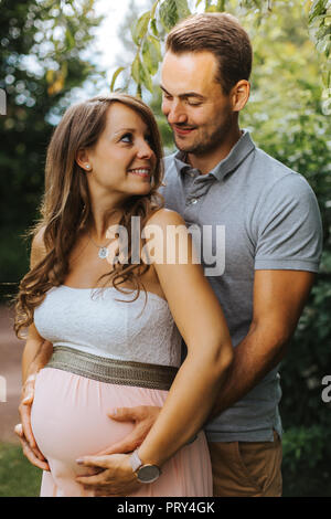 Il marito è abbracciando la sua bella moglie incinta da dietro e toccando il suo ventre Foto Stock