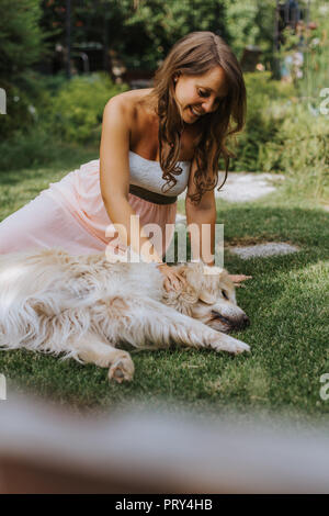 Donna incinta seduta sul prato e giocare con il Golden Retriever Foto Stock