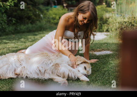 Donna incinta seduta sul prato e giocare con il Golden Retriever Foto Stock