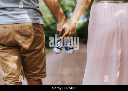 Vista posteriore della coppia a piedi tenendo le mani e portante tiny scarpe per bambini Foto Stock