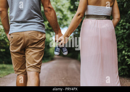 Vista posteriore della coppia a piedi tenendo le mani e portante tiny scarpe per bambini Foto Stock