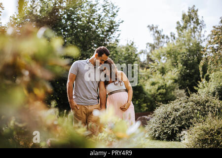 Donna incinta tenendo le mani con il suo partner mentre passeggiate nella natura Foto Stock
