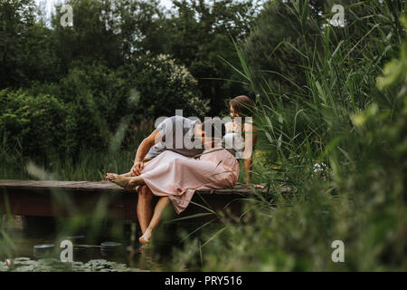 Il marito baci a sua moglie il ventre durante i momenti di relax al lago Foto Stock